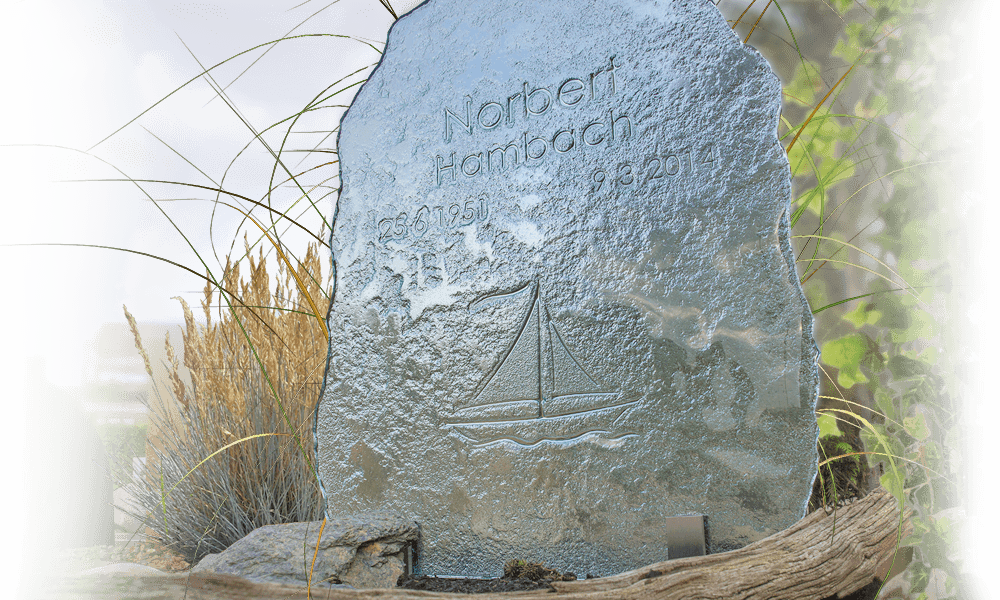 glazen gedenkplaat in monumententuin met grafstenen